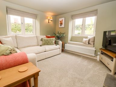 A living room with a beige sofa green cushions window bench with cushions a wall light and a television at 4 Lower Folley in Chipping Campden