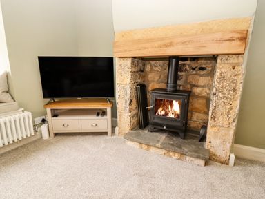 A living room corner with a stone fireplace with a wood-burning stove and a television on a wooden stand at 4 Lower Folley in Chipping Campden