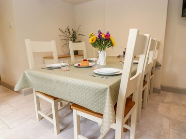 A dining table with six chairs plates glasses flowers and a cake at 4 Lower Folley in Chipping Campden