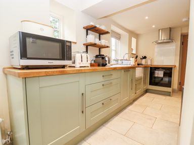 A kitchen with green cabinets wooden countertops a microwave toaster coffee machine and oven at 4 Lower Folley in Chipping Campden