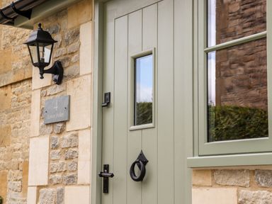 A green door with a black door knocker and handle next to a stone wall with a lantern and a plaque that reads 4 Lower Folley at 4 Lower Folley in Chipping Campden