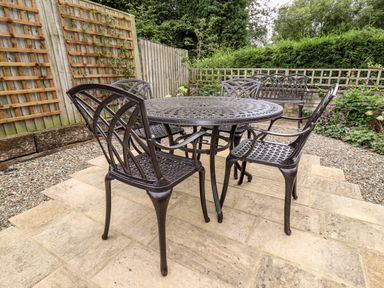 A patio with metal table and chairs near a wooden fence with plants at 4 Lower Folley in Chipping Campden
