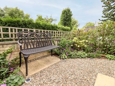 A garden bench on a stone slab surrounded by gravel and plants at 4 Lower Folley in Chipping Campden