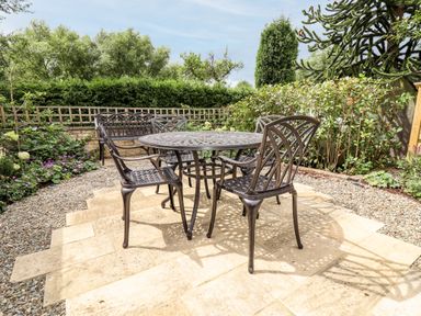 A garden patio with a metal table and four chairs surrounded by plants and shrubs at 4 Lower Folley in Chipping Campden