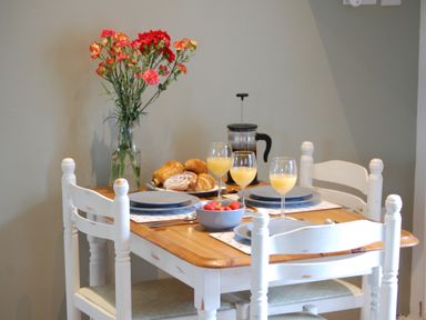 A dining table set with plates glasses of orange juice a bowl of strawberries a plate of pastries and a vase with flowers at Carreg Cennen Cottage in Llandeilo
