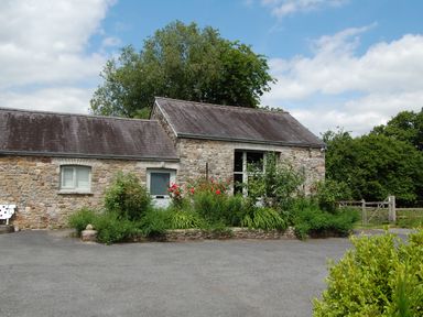 A stone house with two gray doors and a garden with flowers in front at Carreg Cennen Cottage in Llandeilo