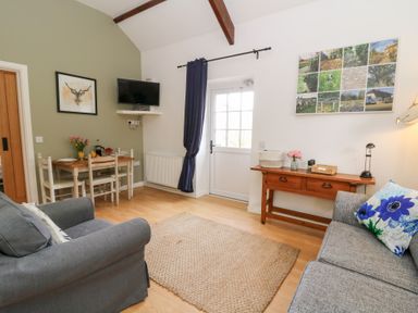 A living room with two sofas a wooden table with chairs a wall-mounted tv and a door at Carreg Cennen Cottage in Llandeilo