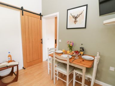 A dining area with a wooden table set for three people with plates glasses of juice flowers and fruit bowl at Carreg Cennen Cottage in Llandeilo