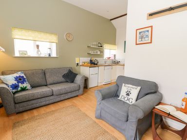 A living area with a grey sofa, armchair, small kitchen with appliances and shelves at Carreg Cennen Cottage in Llandeilo