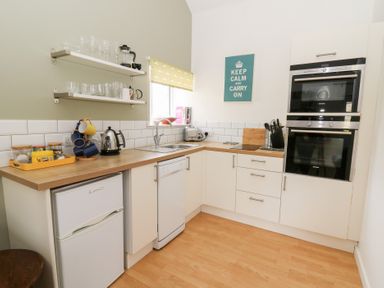 A kitchen with white cabinets wooden countertops and appliances at Carreg Cennen Cottage in Llandeilo