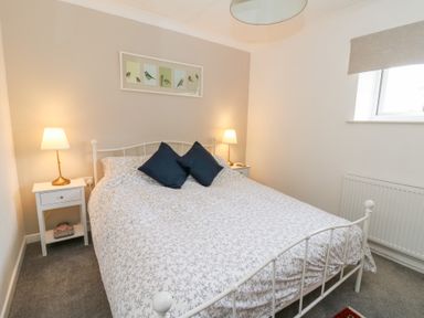 A bedroom with a white metal bed frame two bedside tables with lamps and a framed bird print on the wall at Carreg Cennen Cottage in Llandeilo