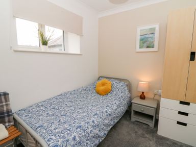 A bedroom with a single bed with patterned bedding a nightstand with a lamp a wardrobe and a window with a plant at Carreg Cennen Cottage in Llandeilo