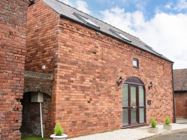 A brick building with an arched glass door and small planters outside at The Little Beehive in Abberley