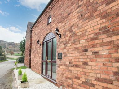 Exterior of a brick building with glass double doors and potted plants at The Little Beehive in Abberley
