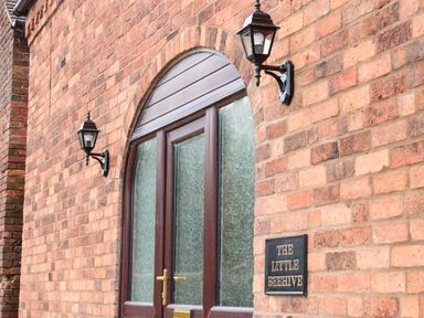 A brick wall with two lamps and an arched door with frosted glass at The Little Beehive in Abberley