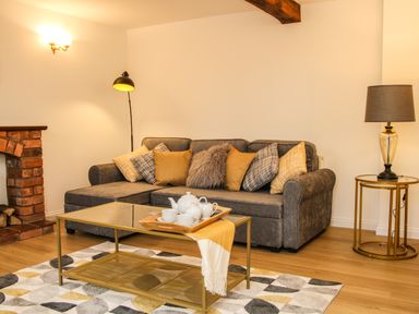 A living room with a gray sofa with cushions a glass coffee table with tea set a floor lamp and a side table lamp at The Little Beehive in Abberley