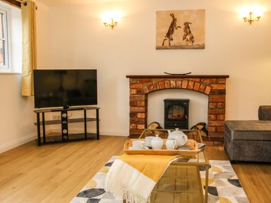 A living room with a television on a stand fireplace and tea set on a glass coffee table at The Little Beehive in Abberley