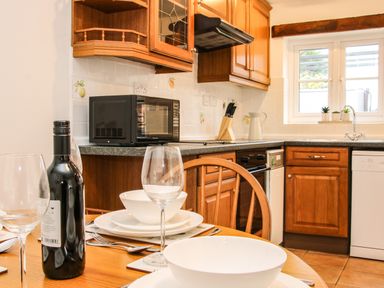 A kitchen with wooden cabinets a microwave oven a wine bottle and glasses on a dining table at The Little Beehive in Abberley