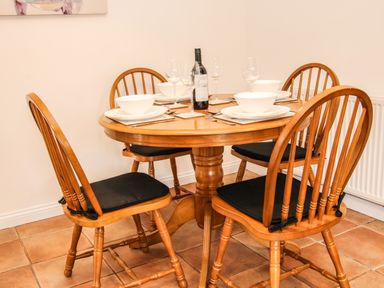 A wooden dining table set for four with plates bowls wine glasses and a bottle of wine at The Little Beehive in Abberley