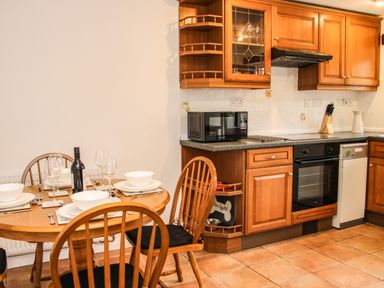 A kitchen with wooden cabinets a black microwave a stove and a dining table set with dishes and wine at The Little Beehive in Abberley