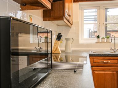 A kitchen counter with a microwave, knife block, ceramic jug and window above a sink at The Little Beehive in Abberley