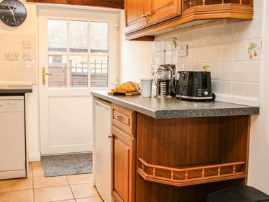 A kitchen countertop with a toaster a French press a mug and sliced bread near a door with a clock on the wall at The Little Beehive in Abberley