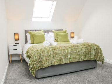 A bedroom with a double bed green pillows and blanket bedside tables with lamps at The Little Beehive in Abberley