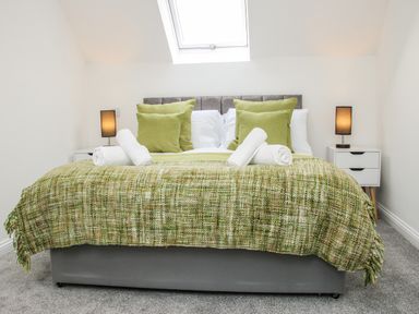 A bedroom with a bed covered with green blankets and pillows and two bedside tables with lamps at The Little Beehive in Abberley