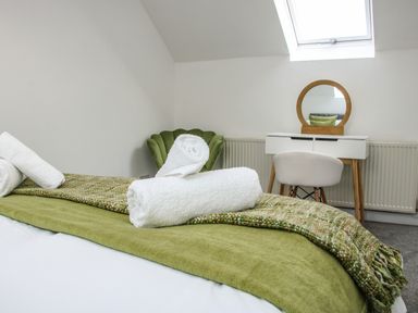 A bedroom with a bed covered in green blankets and white towels and a white vanity table with a round mirror at The Little Beehive in Abberley