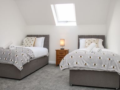 A bedroom with two single beds a wooden nightstand with a lamp and a skylight window at The Little Beehive in Abberley