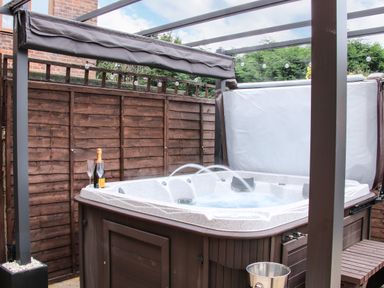 An outdoor hot tub with water jets and a champagne bottle with glasses on the edge at The Little Beehive in Abberley