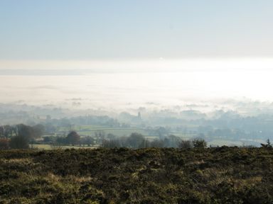 A hilly landscape with shrubs and trees overlooking foggy fields and distant hills at The Little Beehive in Abberley