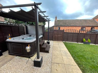 An outdoor hot tub with a canopy and champagne glasses near a paved path and grassy lawn at The Little Beehive in Abberley