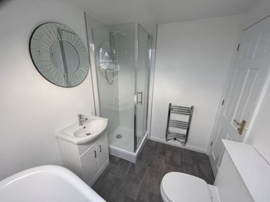 A bathroom with a shower cubicle sink with cabinet round mirror toilet and towel radiator at The Little Beehive in Abberley