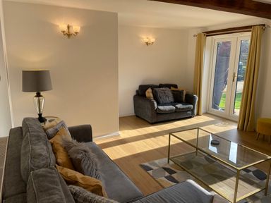 A living room with grey sofas pillows glass coffee table lamp and glass doors with yellow curtains at The Little Beehive in Abberley