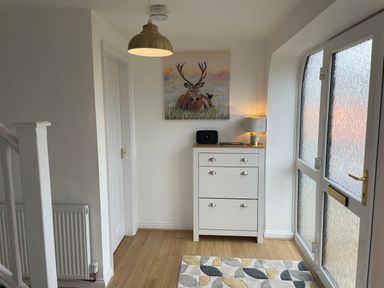 An entryway with a white cabinet, a lamp, a radio, a painting of a deer, a rug, a frosted glass door, and a staircase at The Little Beehive in Abberley