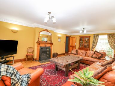 A living room with leather sofas wooden coffee table fireplace and television at The Firs in Wendling near Dereham