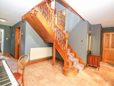 A hallway with wooden staircase carpeted steps a piano and chair with tiled floor at The Firs in Wendling near Dereham
