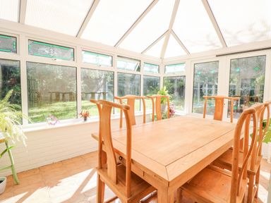 A dining area with wooden table and chairs in a conservatory with plants on the windowsill at The Firs in Wendling near Dereham
