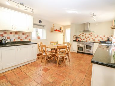 A kitchen with a wooden table and chairs a stove cabinets and tiled floor at The Firs in Wendling near Dereham