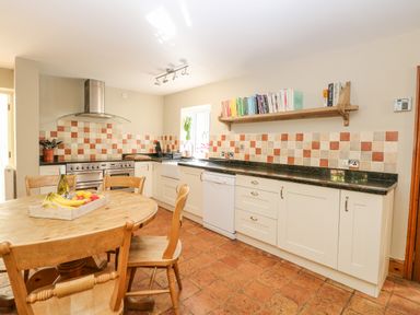 A kitchen with wooden table and chairs tiled floor and backsplash and white cabinets at The Firs in Wendling near Dereham
