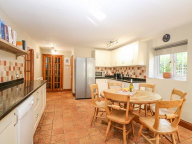 A kitchen with a round wooden table and six chairs next to a window and white cabinets with appliances at The Firs Wendling near Dereham