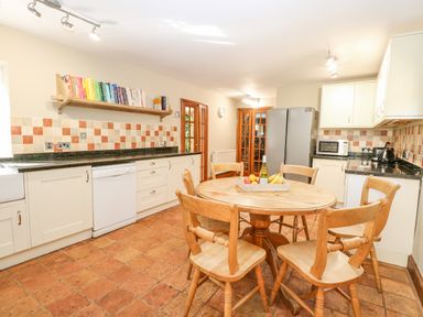 A kitchen with a round wooden table and chairs a refrigerator and a bookshelf with books at The Firs in Wendling near Dereham