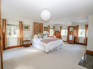 A bedroom with a bed bedside tables dressers and windows with curtains at The Firs in Wendling near Dereham