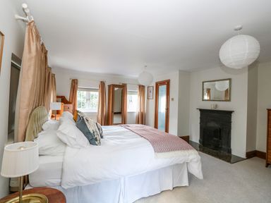 A bedroom with a large bed white bedding a fireplace two windows with curtains a wardrobe and a mirror at The Firs in Wendling near Dereham