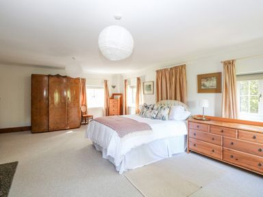 A bedroom with a bed pillows dressers and windows with curtains at The Firs in Wendling near Dereham