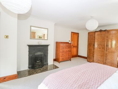 A bedroom with a bed covered in a patterned blanket a wooden chest of drawers a wooden door a large wooden wardrobe a black fireplace and a wall mirror at The Firs in Wendling near Dereham