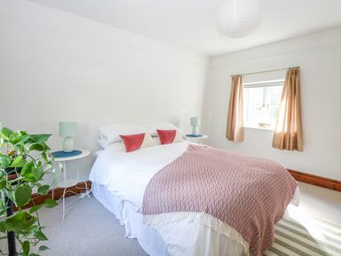 A bedroom with a bed with white bedding and red pillows two side tables with lamps a window with curtains and a plant at The Firs in Wendling near Dereham