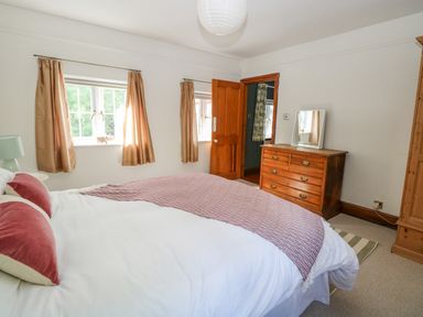 A bedroom with a bed, wooden dresser, windows with curtains, and a wooden door at The Firs in Wendling near Dereham