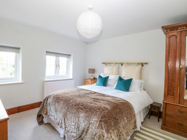 A bedroom with a double bed, bedside tables with lamps, and a wooden wardrobe at The Firs in Wendling near Dereham